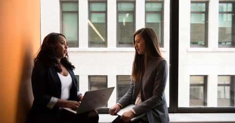 Deux élèves qui se parlent, dont l'une qui a un ordinateur sur les jambes
